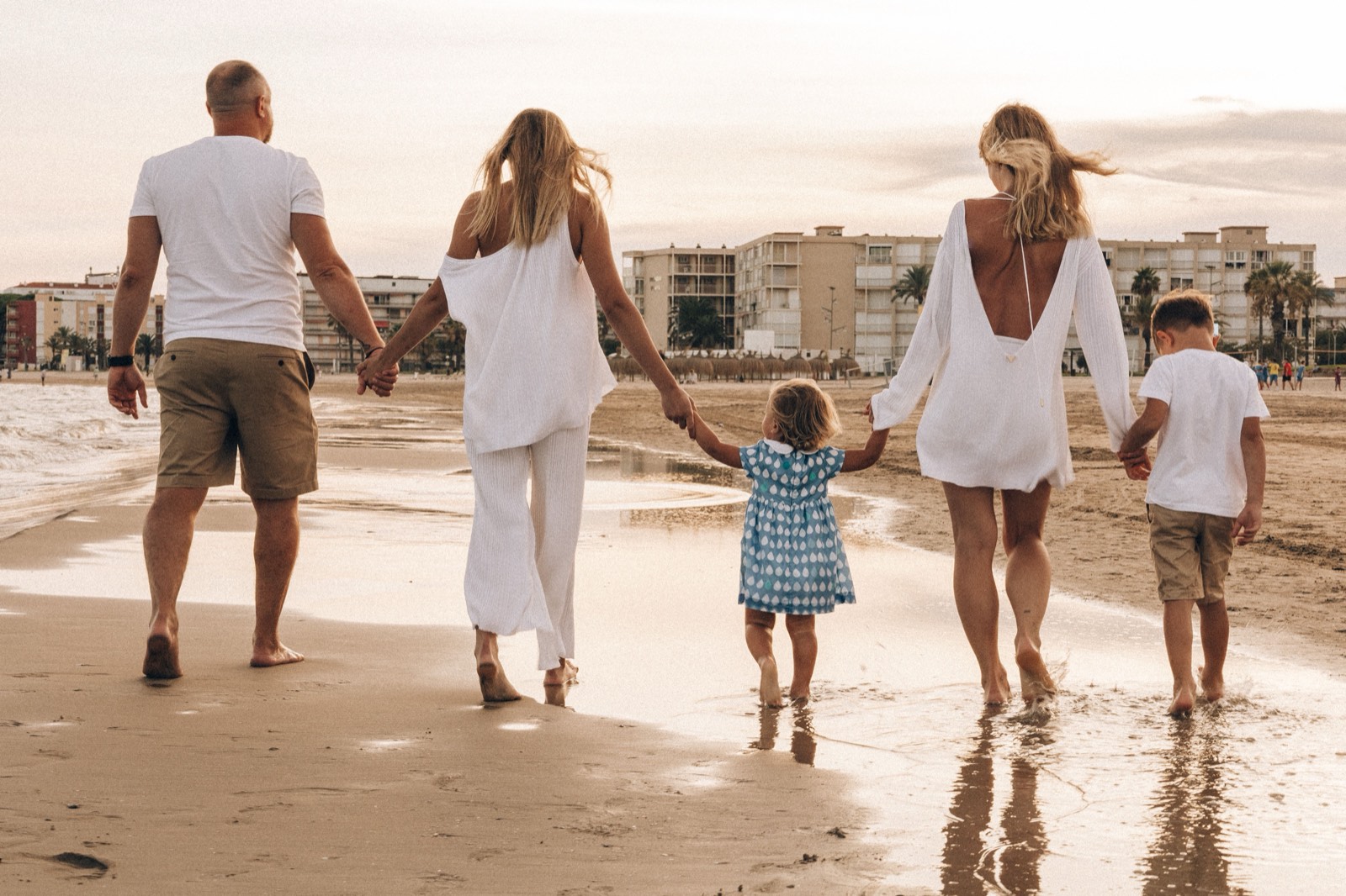 A family of five walking hand in hand along a wet beach at sunset, seen from behind.